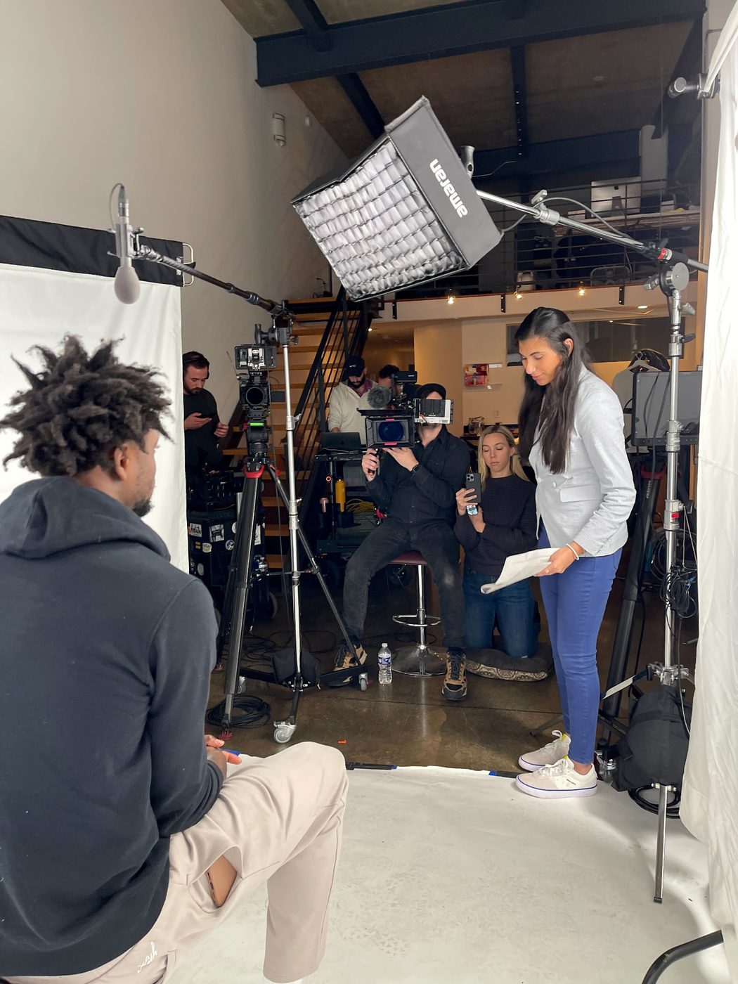 Reilly holding interview notes on a lit set beside camera and audio crew during a shoot